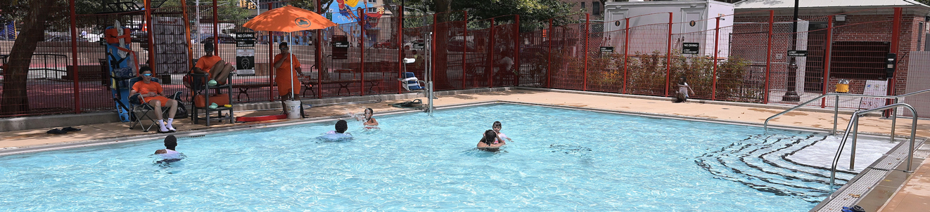 A small pool in a city playground. A few children are playing in the water on a bright sunny day.