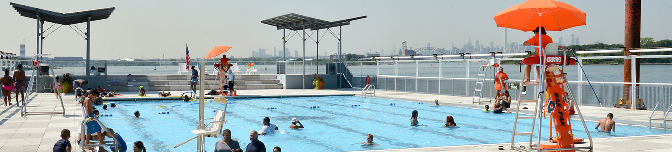 People on a boat using a city pool with the Manhattan skyline in the distance.