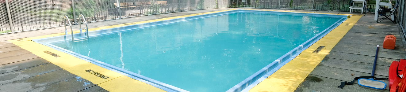 A small quiet pool filled with clear blue water in a neighborhood park.
