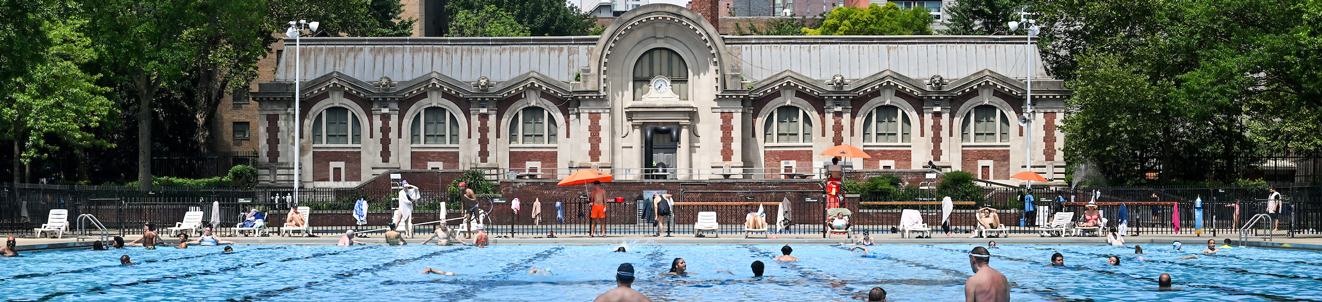 A large outdoor pool with clear blue water in front of an impressive brick building.