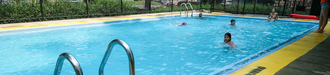 A few kids playing in small city pool in a neighborhood park.