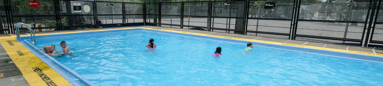 A few families play in a small pool in a city park.