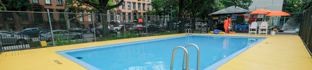 A small pool in a park with a row of Brooklyn brownstones in the background.