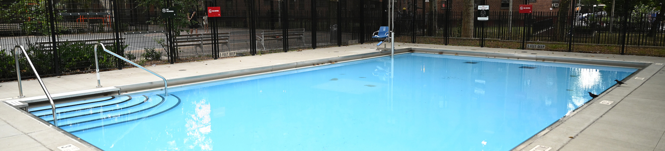 A small, clean, empty pool in a city playground, located near an apartment complex.