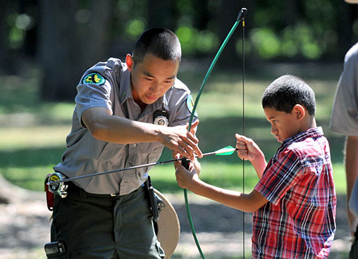 A ranger shows a kid how to use a bow and arrow