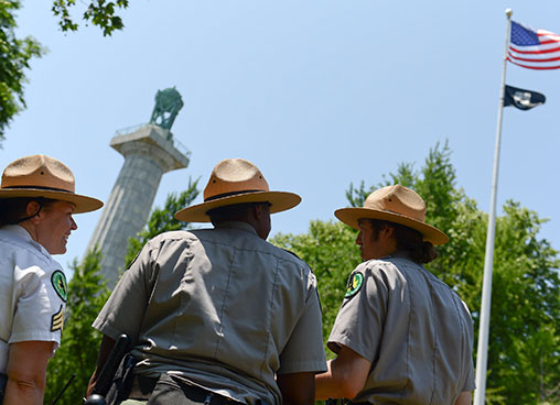 Park rangers walk up to a monument in a park