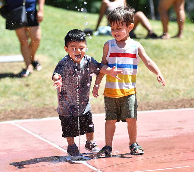 Two children enjoy a spray of water from a spray shower
