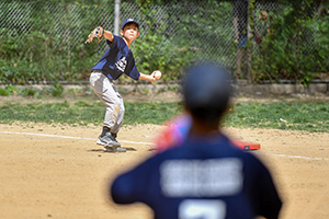 A young baseball pitcher winds up to throw a ball. The batter and catcher are in the foreground.