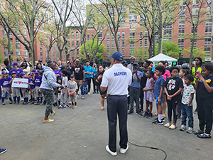 A speaker with a shirt that says "Mayor" on the back presents to a large crowd of children.
