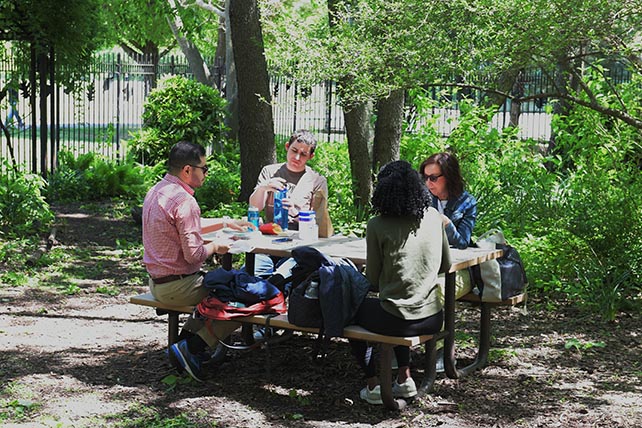 A group of people sitting around a table outside, surrounded by trees.